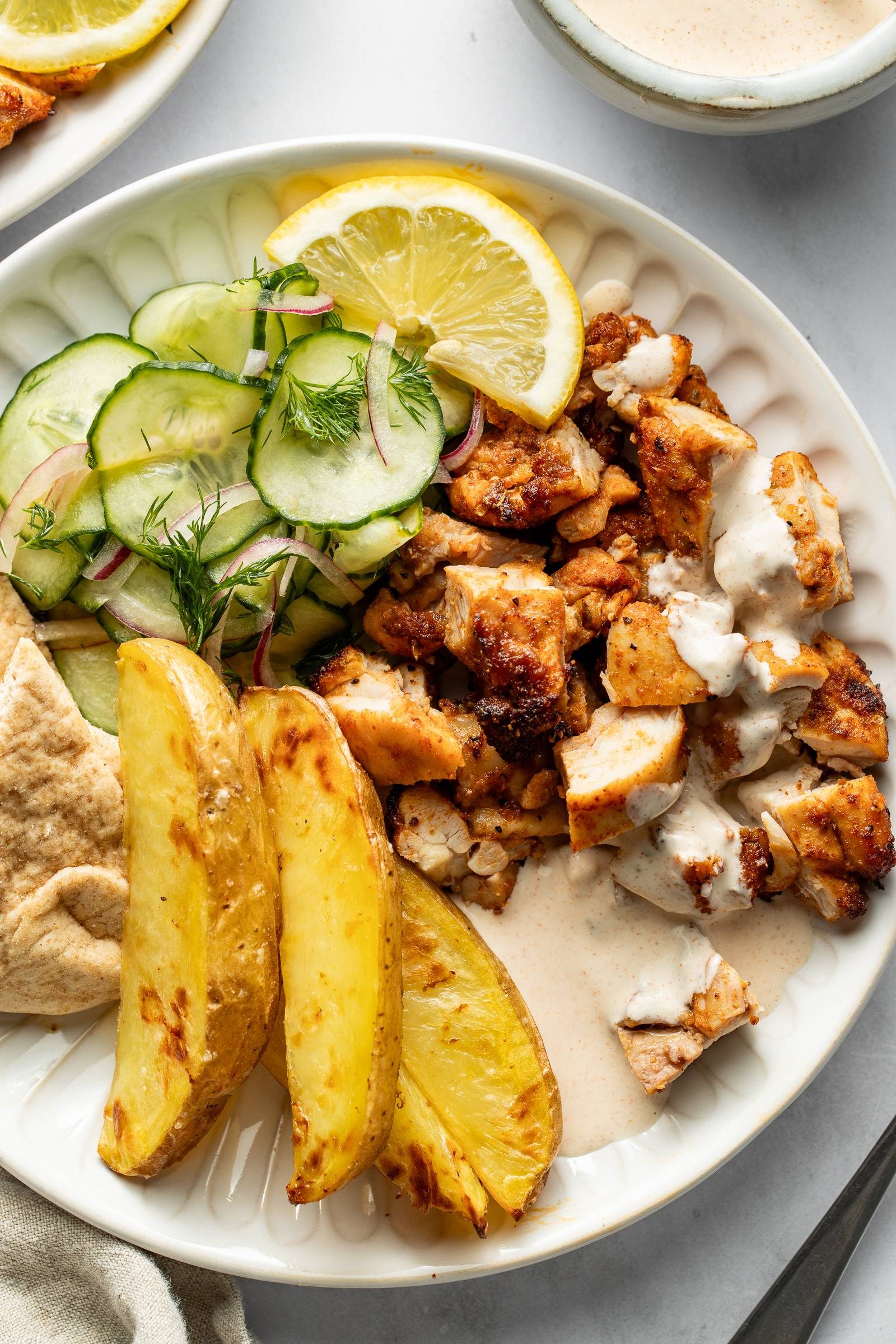 Chicken, potatoes, and cucumber salad on a plate.