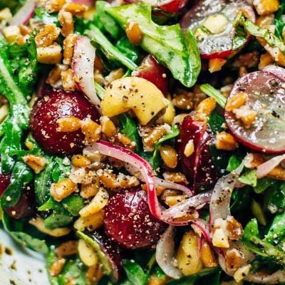 Arugula Salad with grapes, cashews, and pickled red onions in a bowl with a fork.