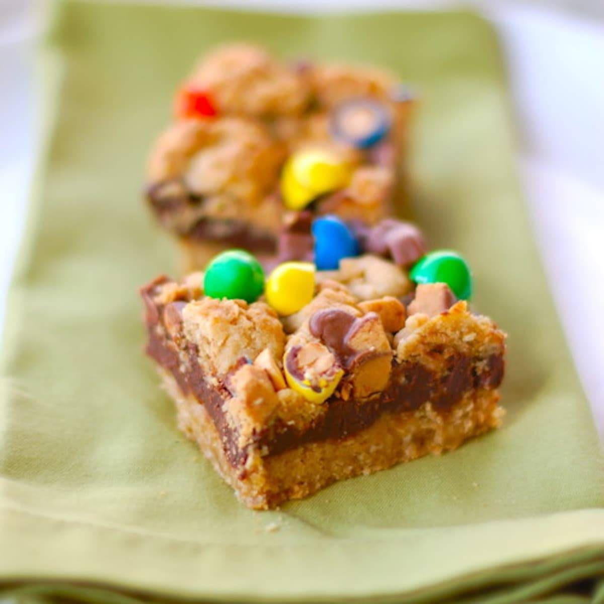 Two candy fudge bars with colorful candy topping on a green napkin.