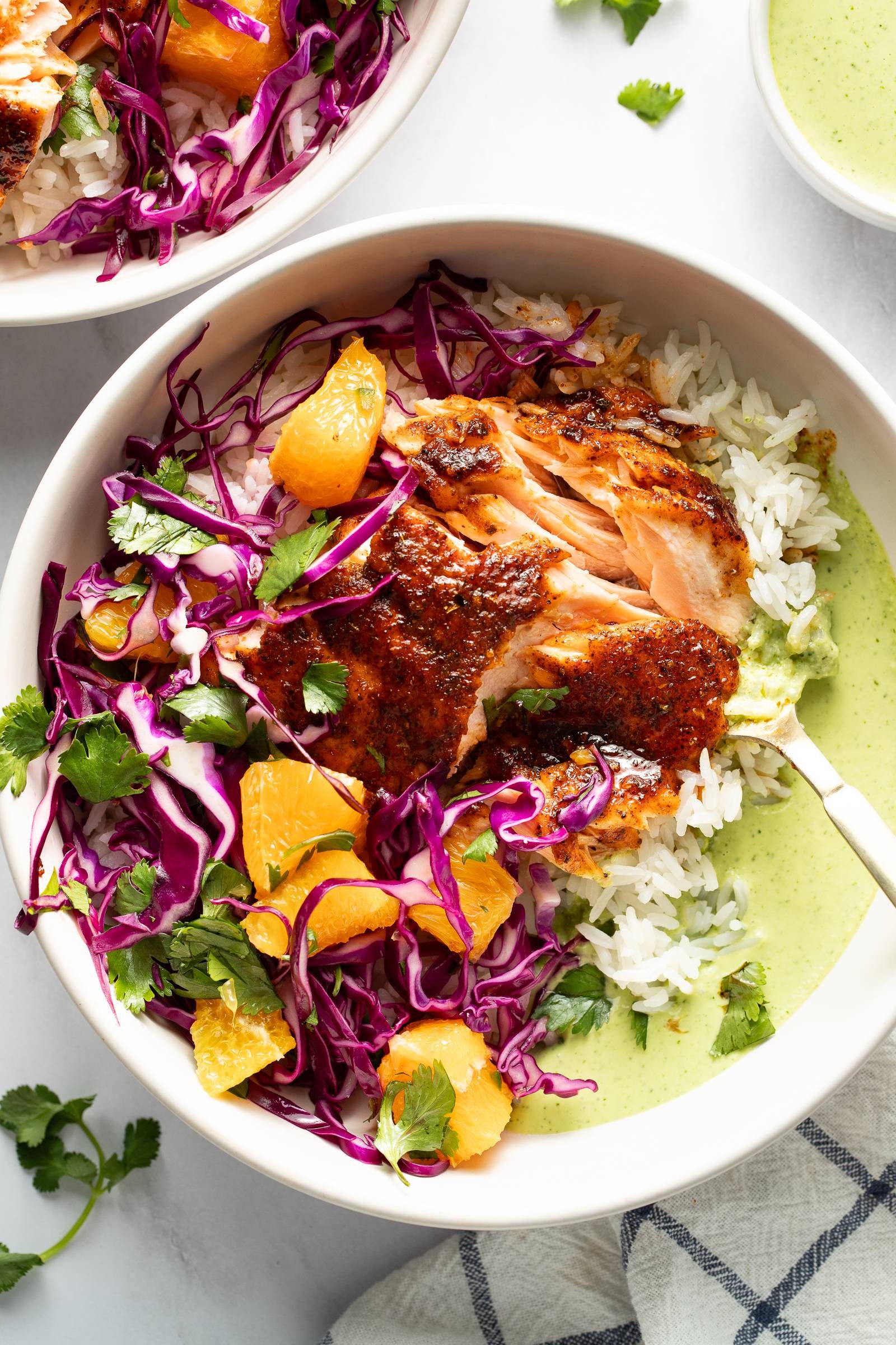 Chipotle salmon in a bowl with rice, orange salsa, slaw, and aji verde sauce.