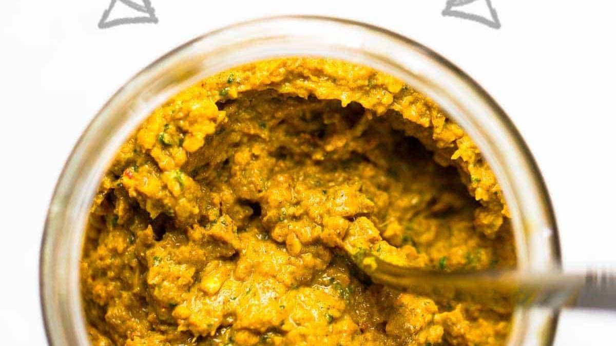 Homemade yellow curry paste in a jar with a spoon.