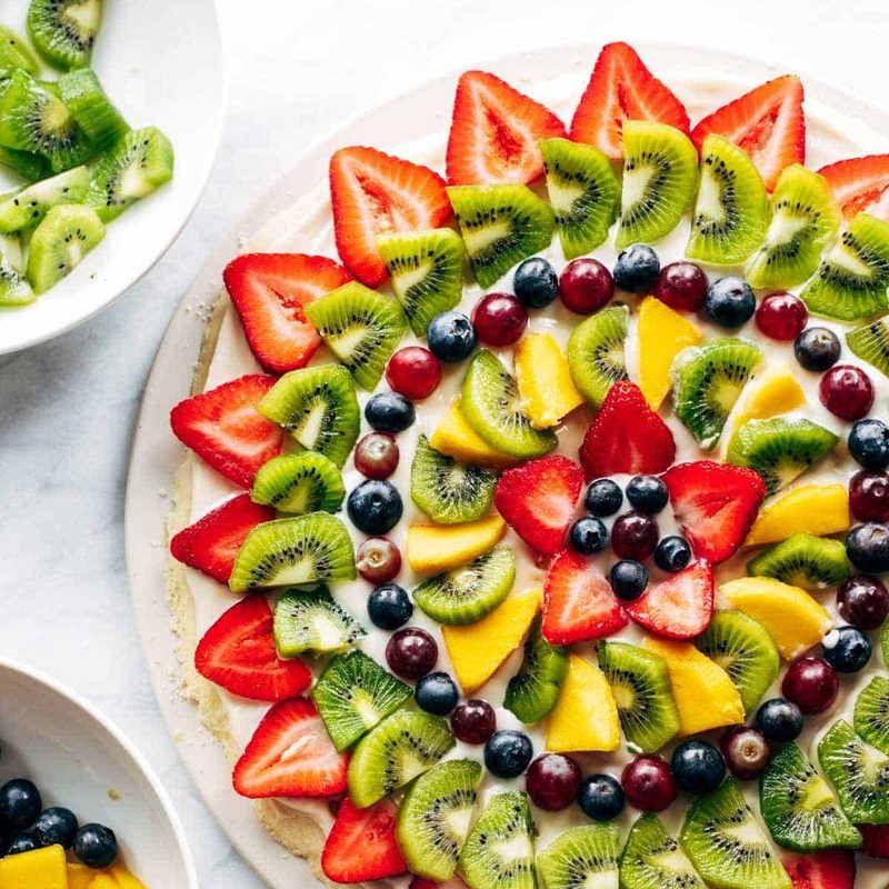 Fruit pizza with bowls of fruit.