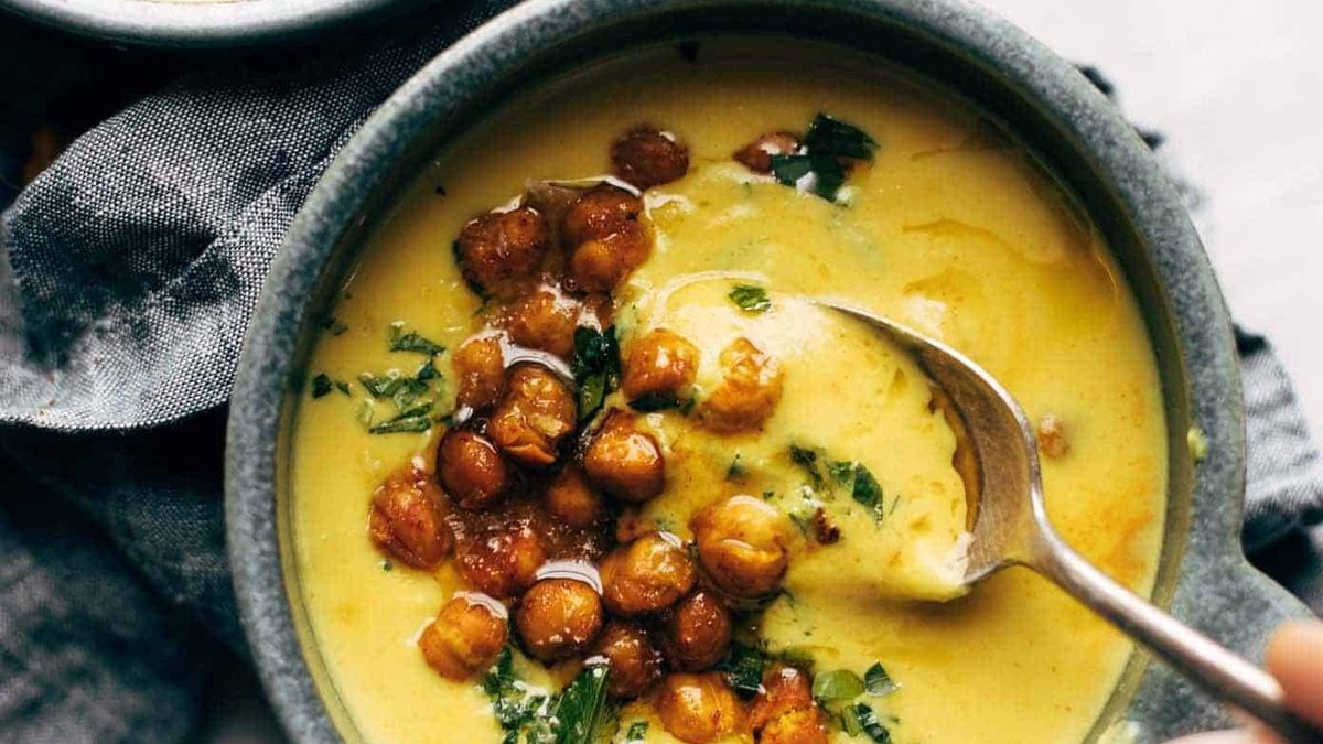 Two bowls of golden soup with roasted chickpeas and olive oil drizzled on top.