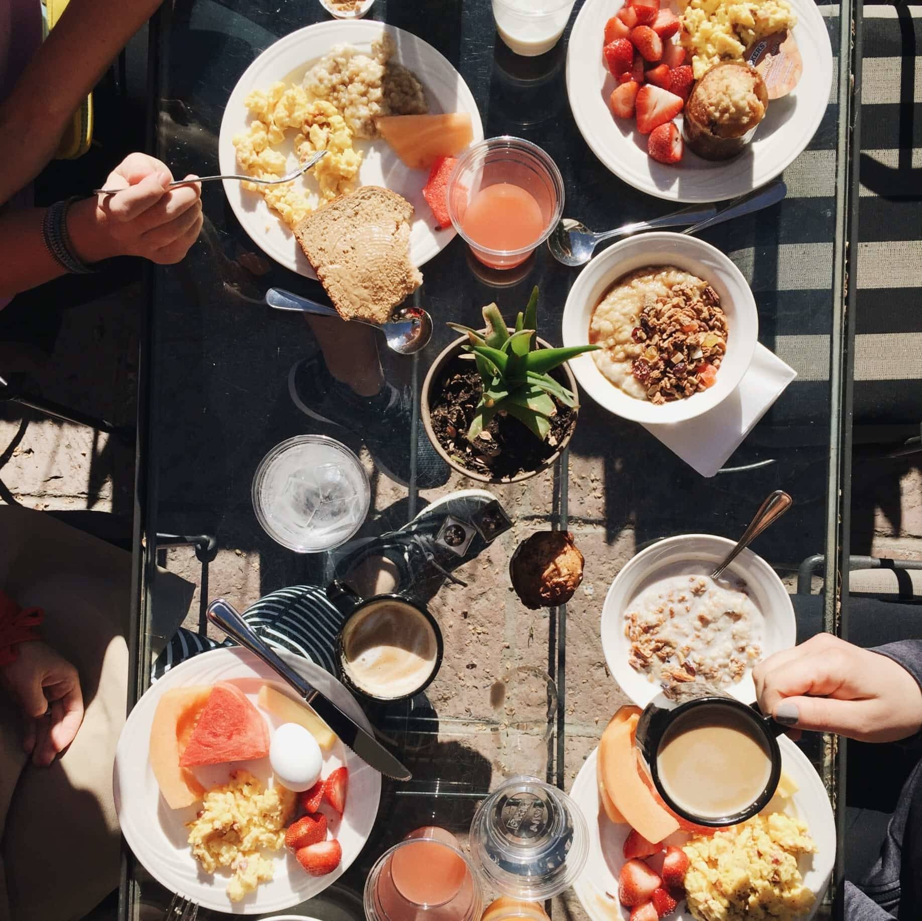 plates with food on a glass table and hands holding forks and coffee