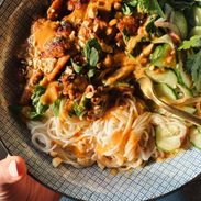 Peanut chicken in a bowl with noodles and herbs.