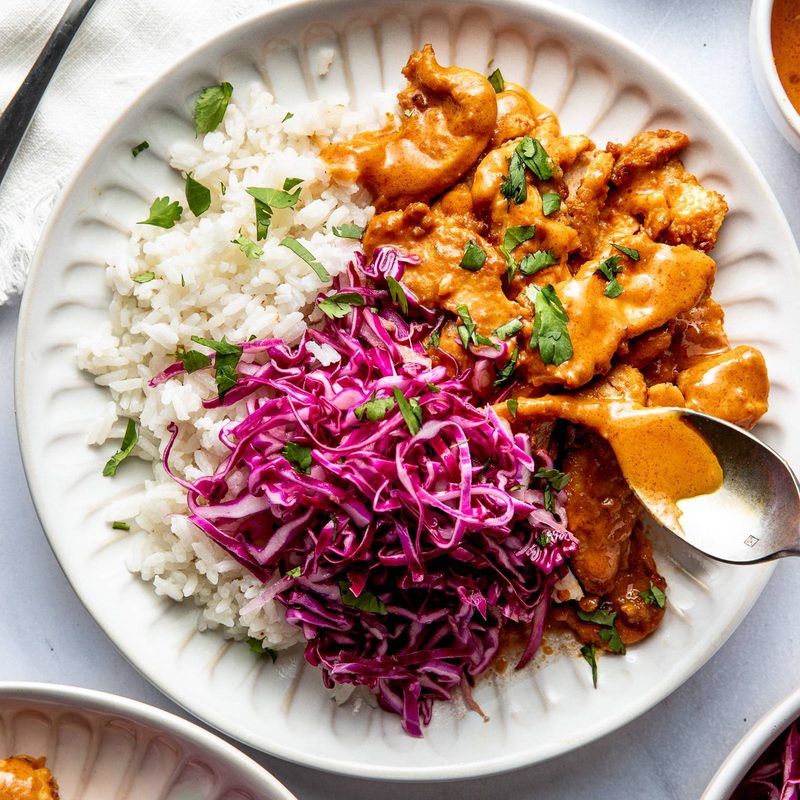 Peanut chicken on a plate with slaw and rice.