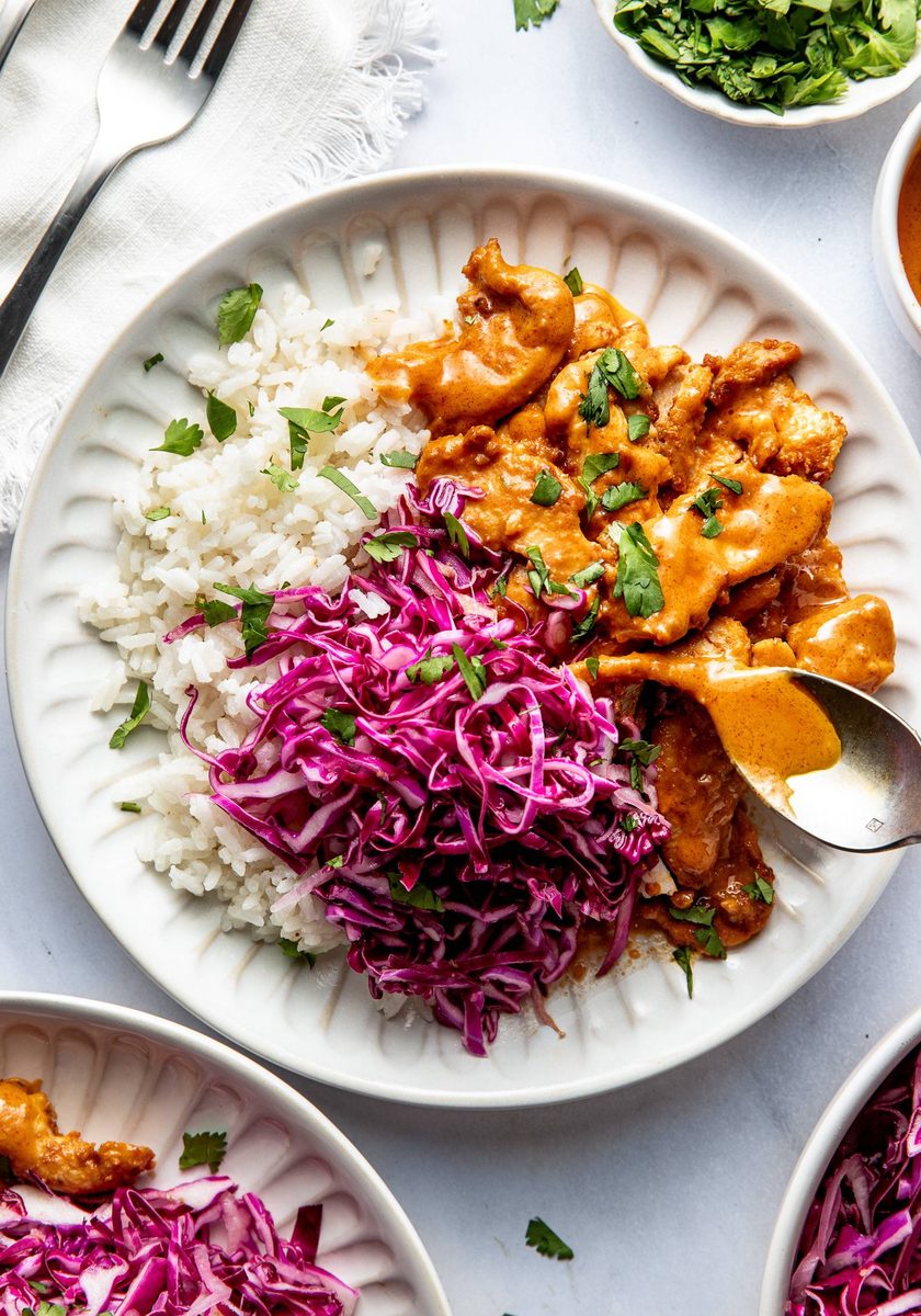 Peanut chicken on a plate with slaw and rice.