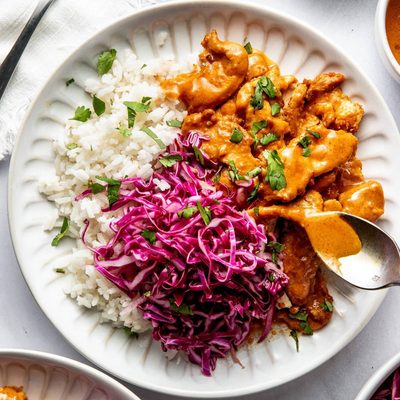 Peanut chicken on a plate with rice and slaw.