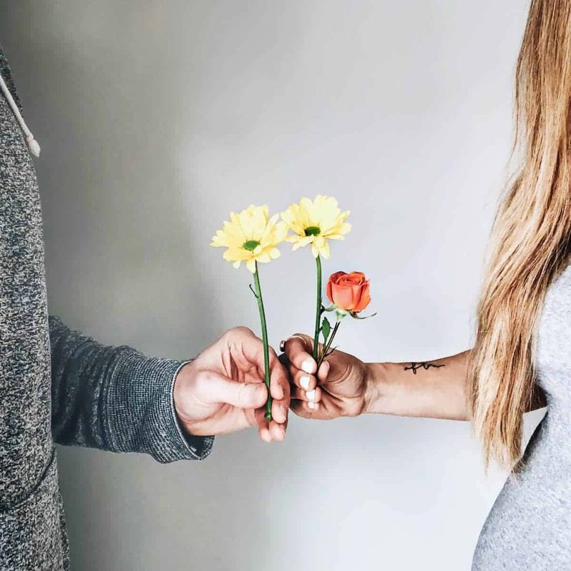 One man and a woman is holding flowers in their hands and holding hands together.