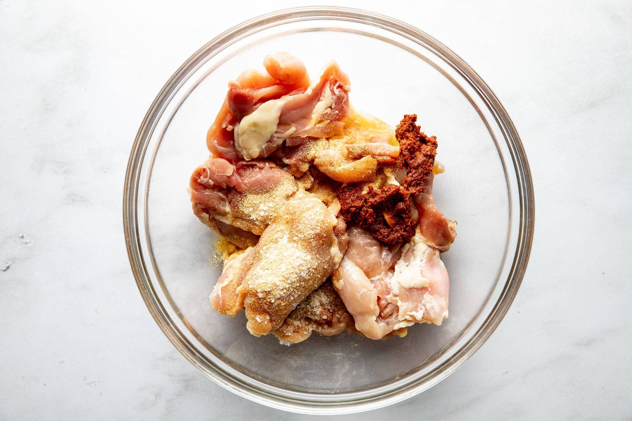 Chicken in a bowl with spices and curry paste.