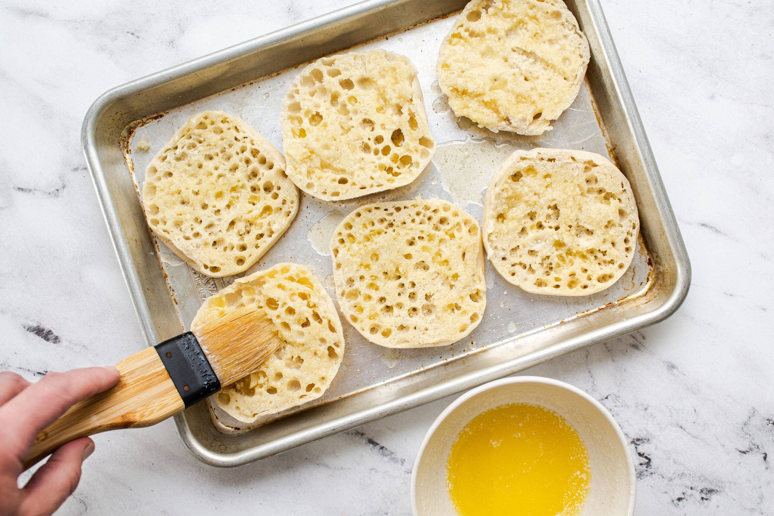 Brushing english muffins with garlic butter.