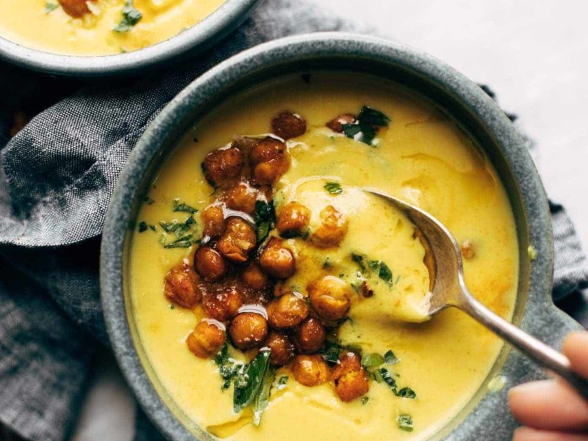 Two bowls of golden soup with roasted chickpeas and olive oil drizzled on top.