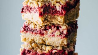 Raspberry crumble bars stacked with a hand.