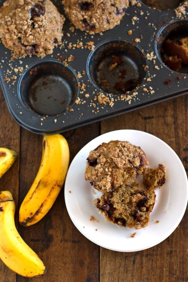 Whole wheat chocolate chip banana peanut butter muffins on a white plate with bananas.