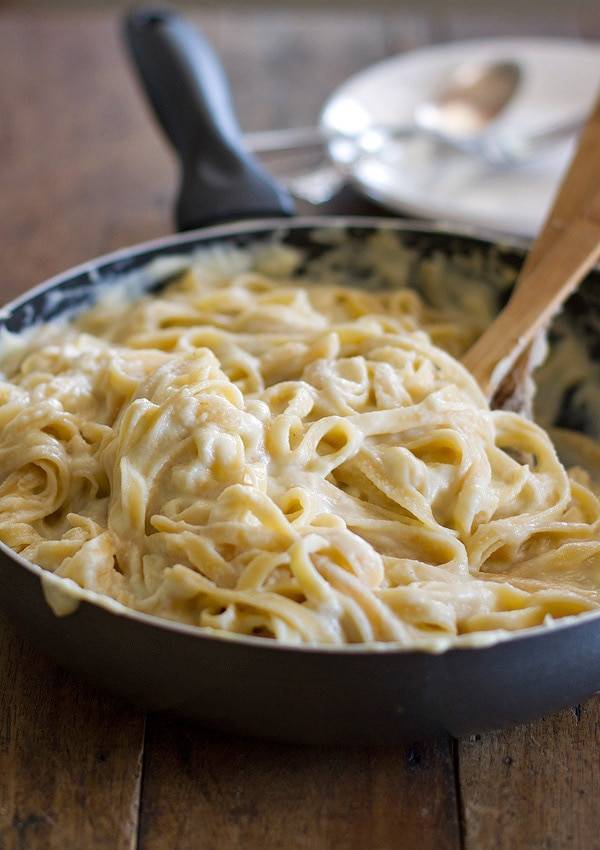 Fettuccine alfredo in a skillet with a wooden spoon.