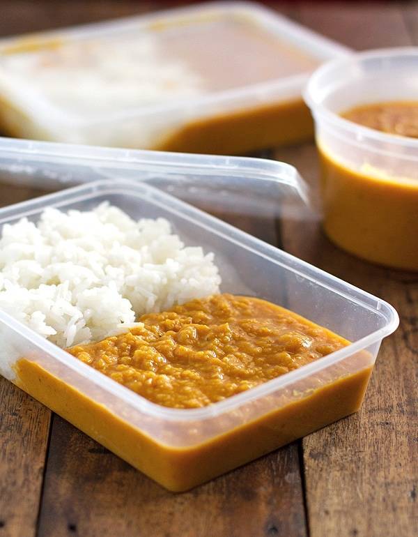 Red lentil dhal with rice in a clear container.