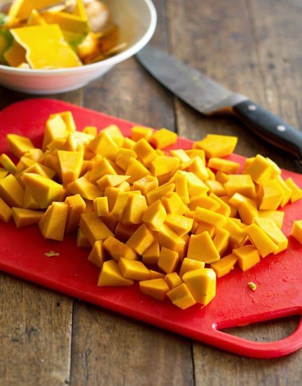 Kabocha squash cut into small pieces on a red cutting board.