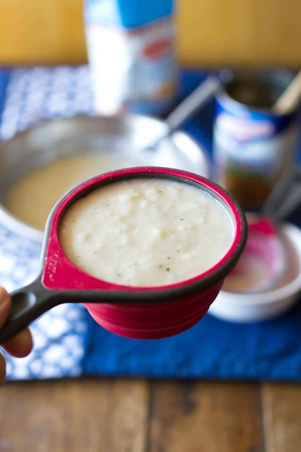 White hand holding a measuring cup filled with cream of chicken soup. 