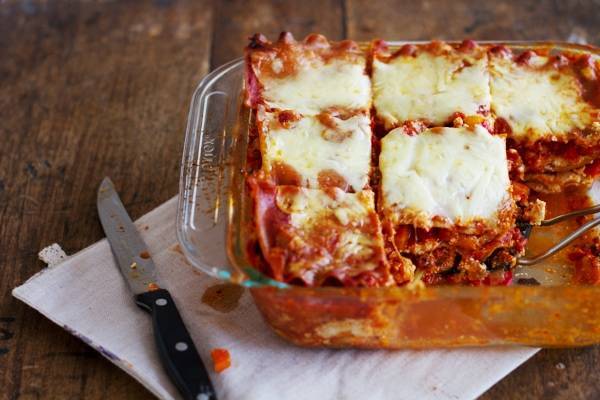 Whole wheat roasted veggie lasagna in a baking dish with a knife.