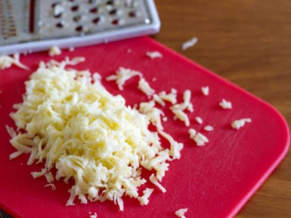 Cheese shreds on a red cutting board.