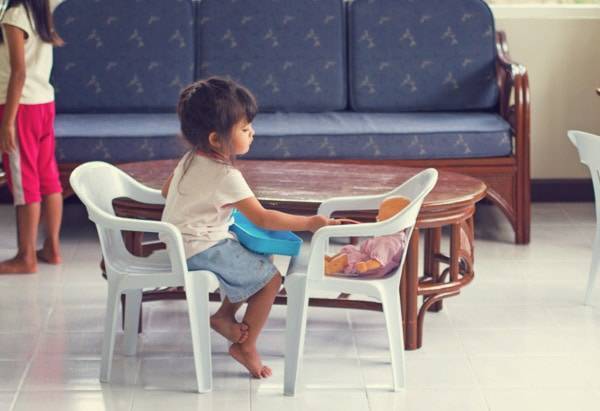 Little girl sitting on a chair playing with a baby.