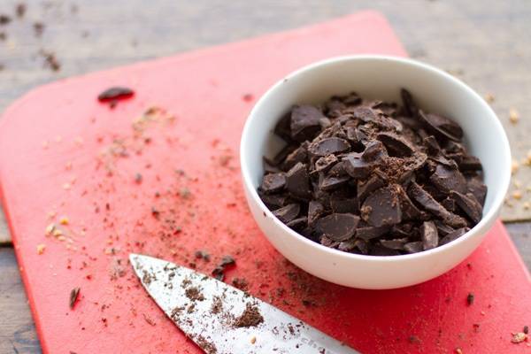 Chocolate chunks in a white bowl and on a red cutting board.