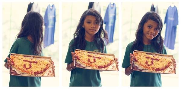Young girl holding an pan of homemade pizza.