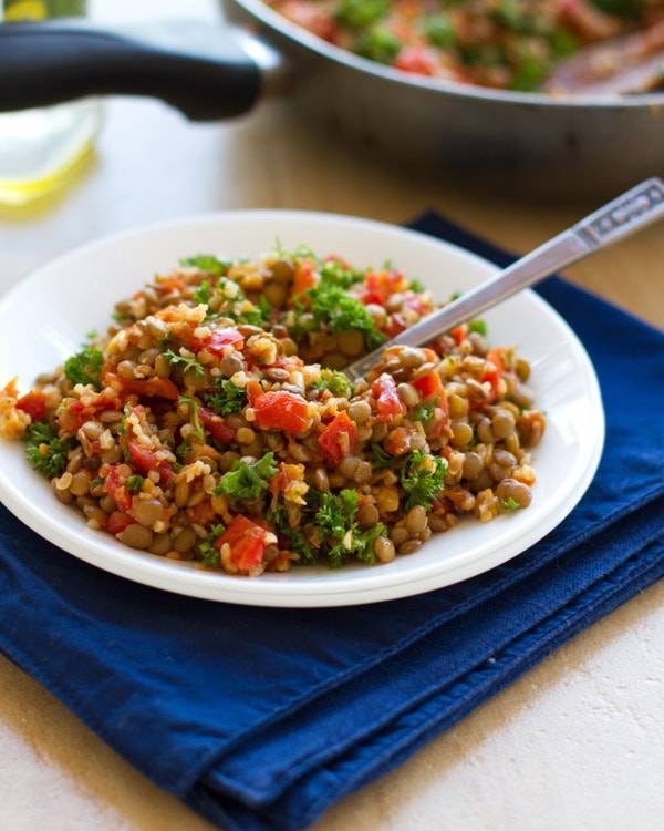 Garlic and tomato lentil salad on a white plate on a blue napkin.
