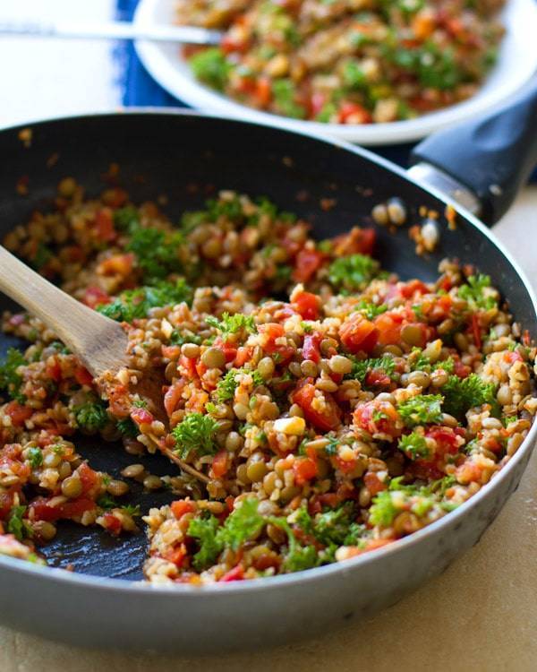 Garlic and tomato lentil salad in a skillet with wooden spoon.