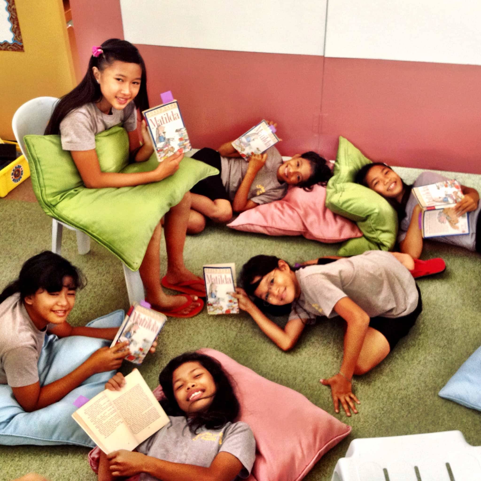 Young girls laying down reading books.