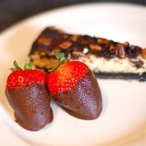Chocolate covered strawberries and cheesecake on a white plate.