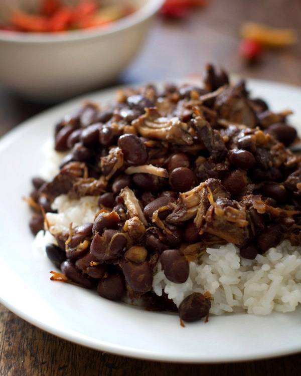 Pork adobo with black beans and rice on a white plate.