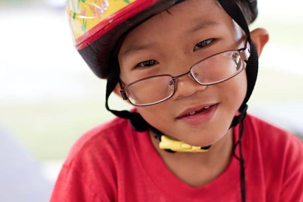 A young boy with glasses and a bike helmet on.
