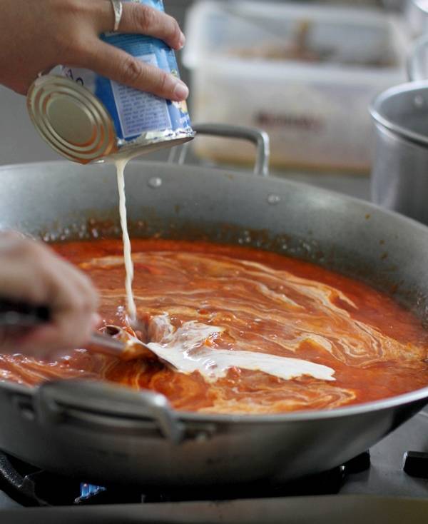 Evaporated milk being poured into sauce for Filipino Spaghetti. 