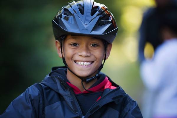 A boy smiling while wearing a jacket and cycling helmet.
