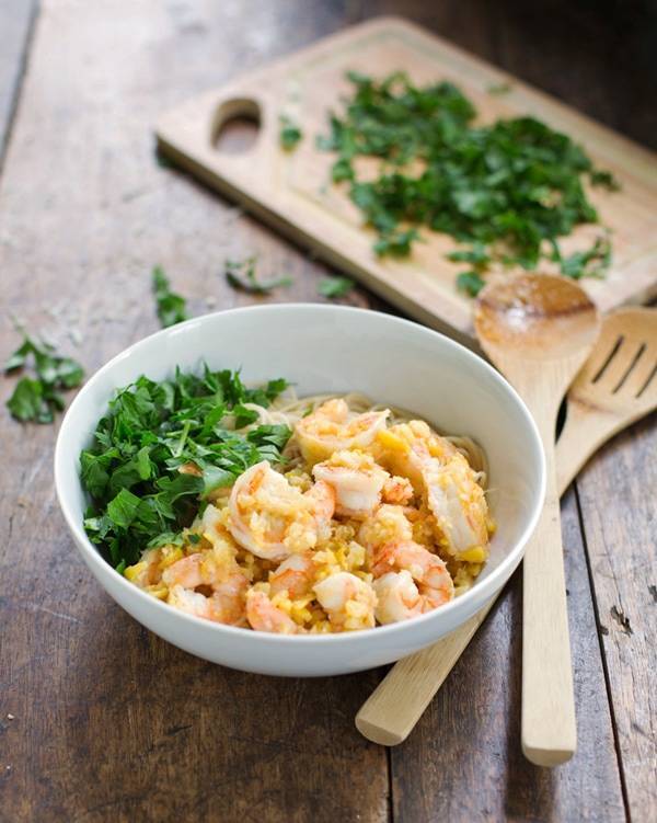 Shrimp scampi in a white bowl with wooden utensils.