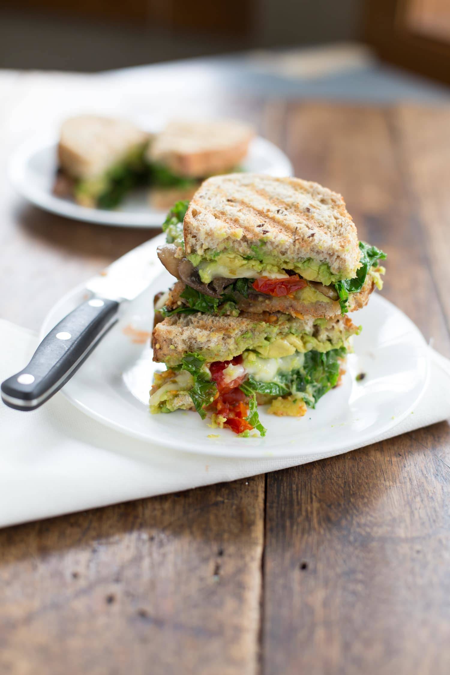 A panini with avocado, roasted red bell peppers, and greens.