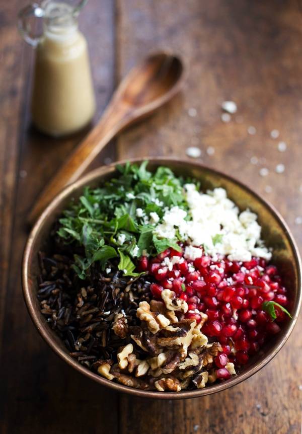 Pomegranate, Kale, and Wild Rice Salad in a bowl with a wooden spoon.