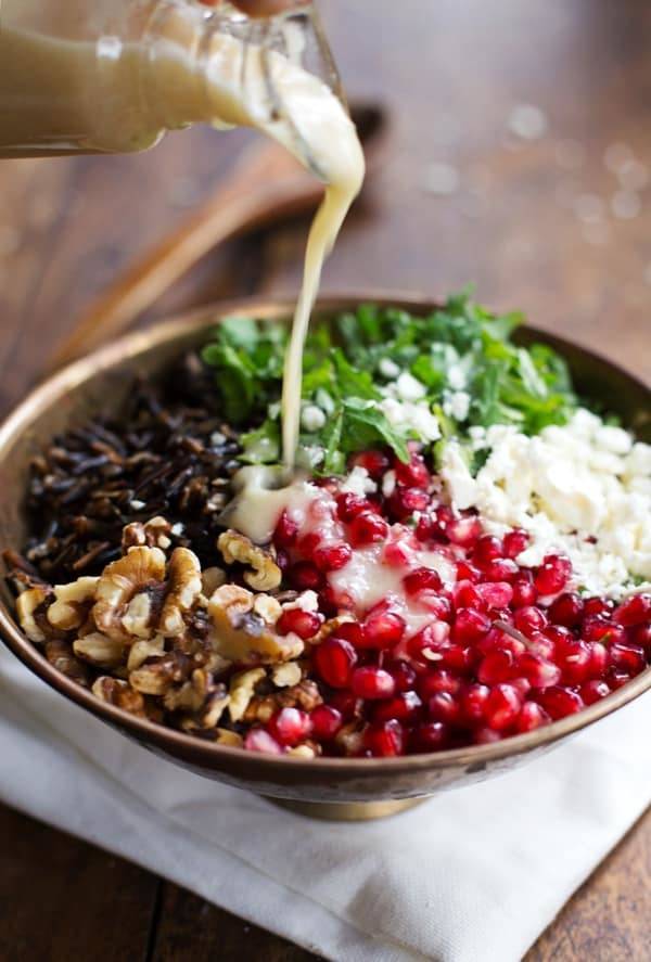 Pomegranate, Kale, and Wild Rice Salad with Walnuts and Feta in a bowl with dressing drizzle.