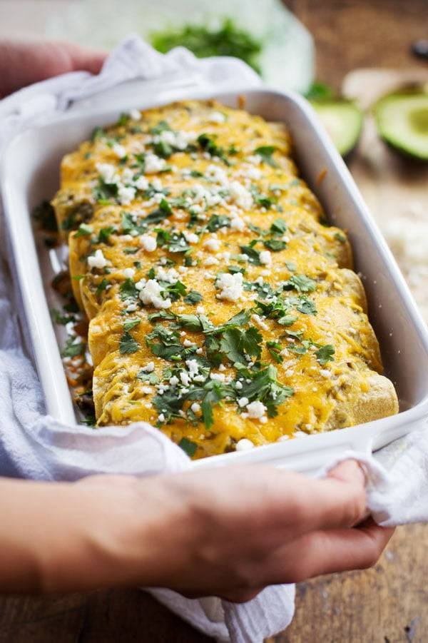 Butternut Squash and Mushroom Enchiladas with Tomatillo Sauce in a white dish.