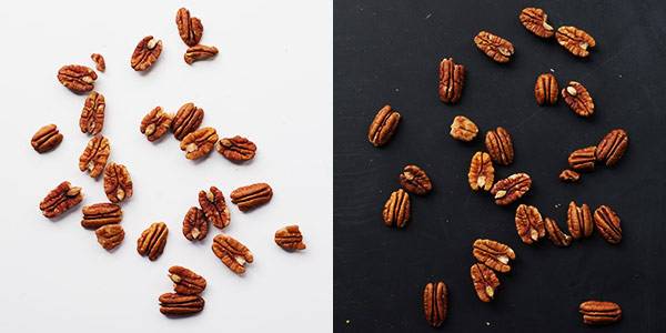 Pecans on a white surface and a black surface.