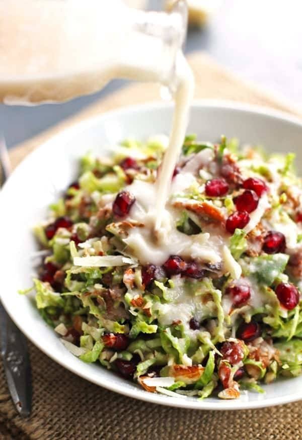 Brussels sprout salad has pomegranates, almonds, crumbled bacon, and homemade creamy salad dressing drizzle.
