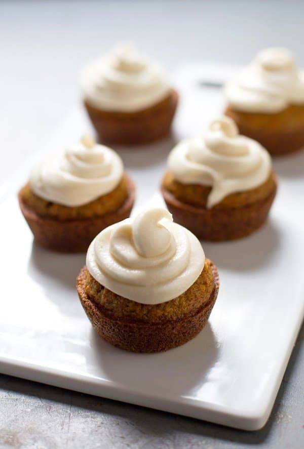 Carrot cake cupcakes with frosting on a white surface.