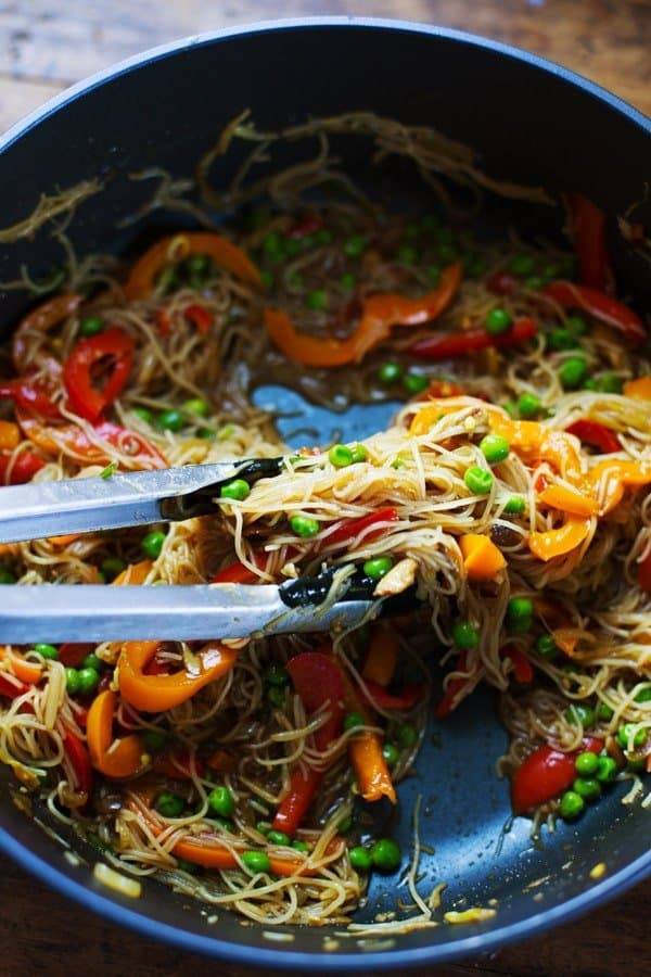 Stir fried Singapore Noodles in a pan with tongs.