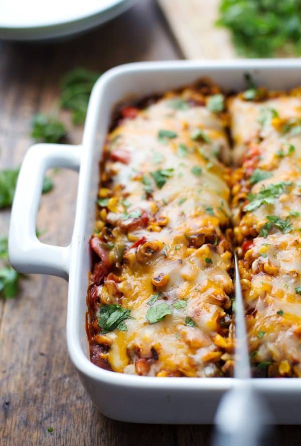 Knife cutting a Mexican casserole in a white pan. 