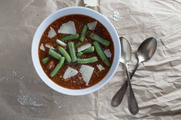 Soup in a bowl with green beans and spoons.