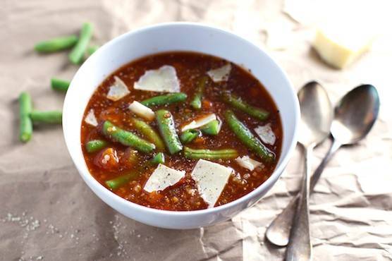 Soup in a white bowl with green beans and spoons.