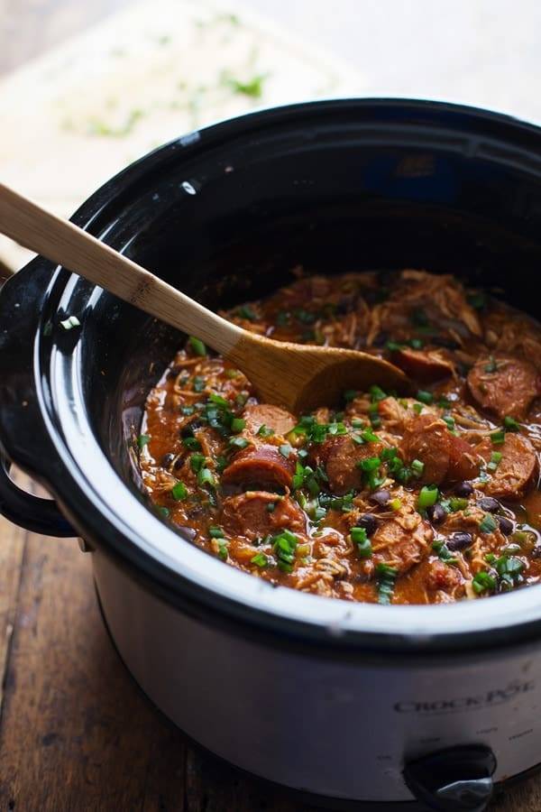 Creole Chicken and Sausage in a crockpot with a wooden spoon.