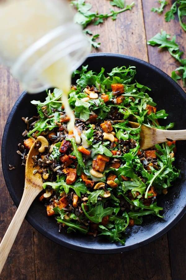 Roasted Sweet Potato, Wild Rice, and Arugula Salad in a bowl with dressing being poured on top