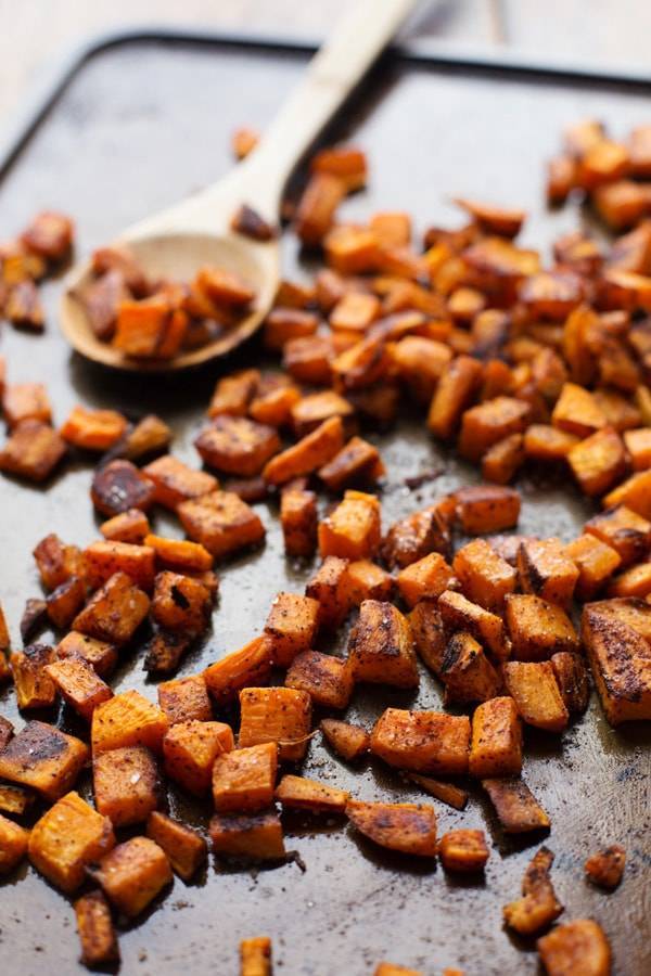 Roasted sweet potatoes on a pan with a wooden spoon.